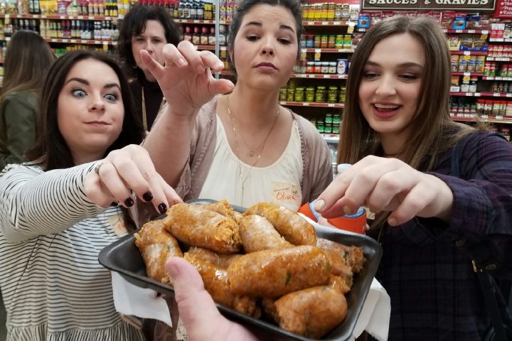 Three women reaching for sausages in a grocery store aisle.