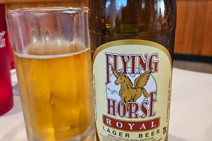 Bottle of Flying Horse Royal Lager Beer next to a glass of beer on a table.
