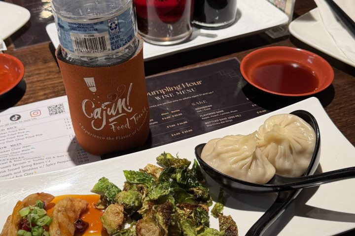 Asian meal with dumplings, Brussels sprouts, sauces, water bottle, and drink on restaurant table.
