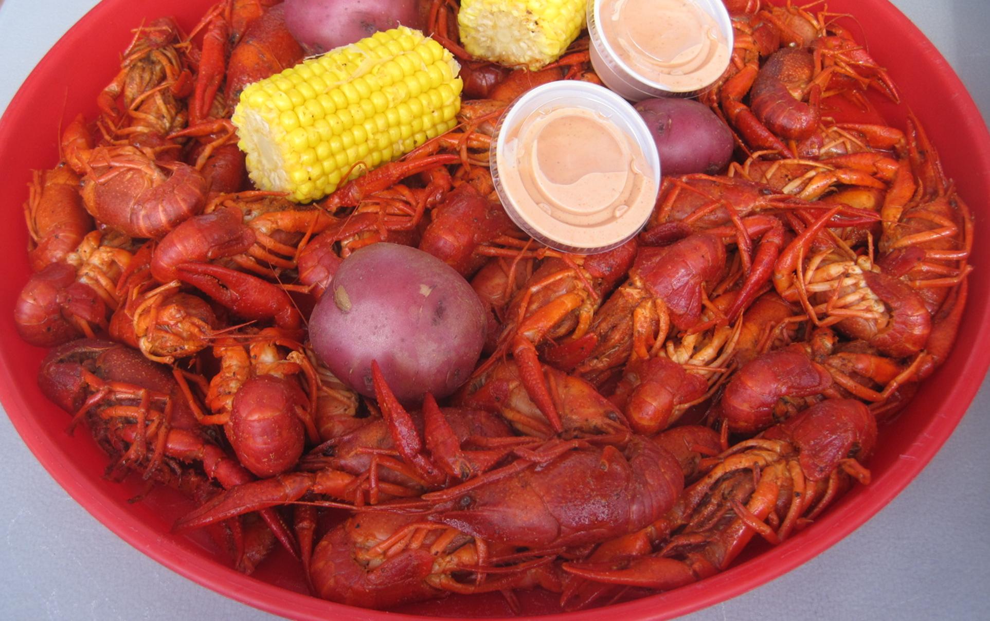 Bowl of cooked crawfish with corn, potatoes, and two sauce cups.